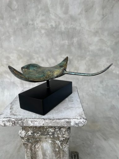 Eine bronzene Skulptur eines stilisierten Vogels auf einem schwarzen Sockel.