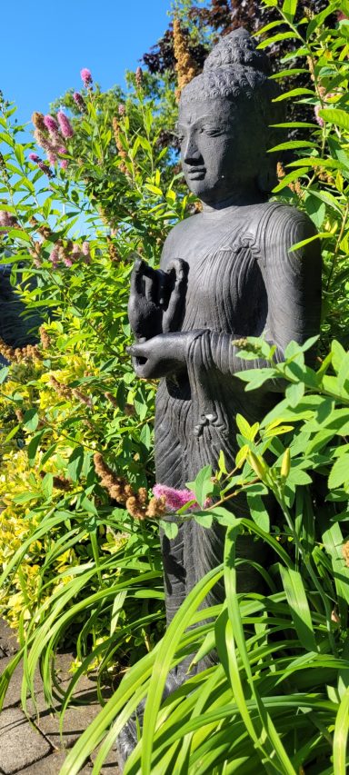 Buddhastatue umgeben von grünen Pflanzen und bunten Blumen im Freien.