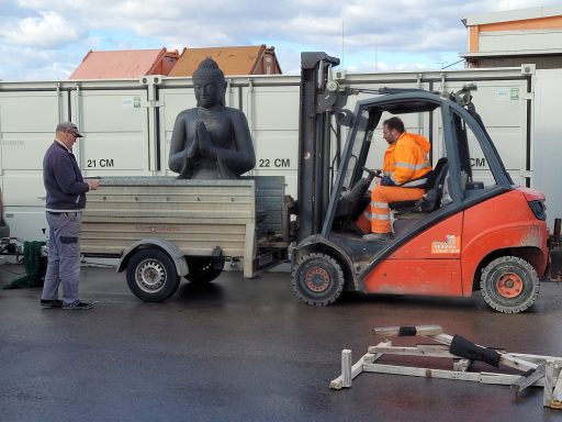Ein Lkw mit einem Buddha-Statue wird von einem Gabelstapler transportiert.