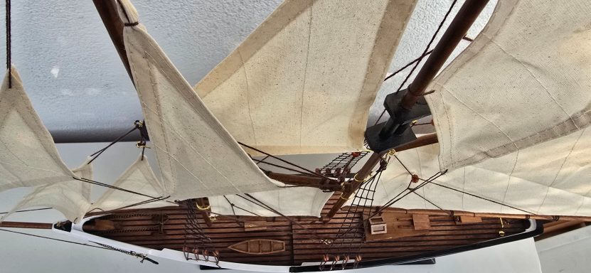 Holzboot mit weißen Segeln, Blick von oben auf Masten und Segel.