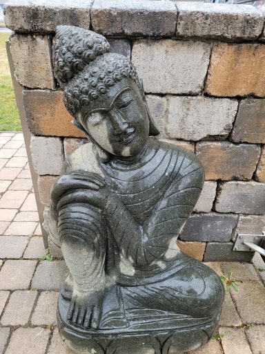 Dunkle Buddha-Statue, sitzend mit geschlossenen Augen, umgeben von Steinen.