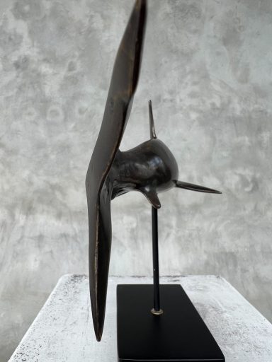 Skulptur eines stilisierten Flugzeugs in metallischer Optik auf schwarzem Sockel.