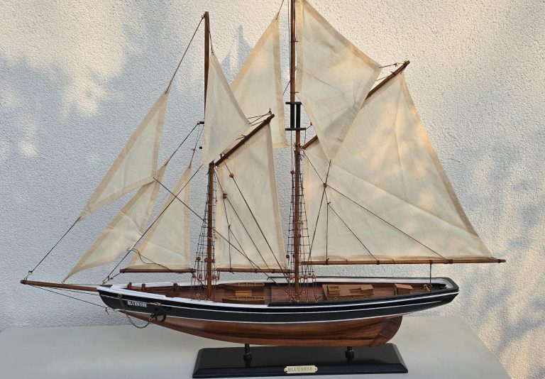 Modell eines Segelboots mit weißen Segeln und Holzdetails auf schwarzem Standfuß.