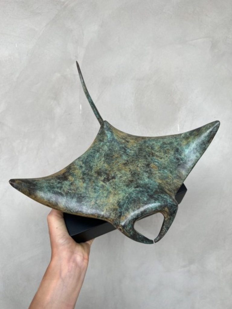 Bronzeskulptur eines Mantas mit spitzen Flossen, in Hand gehalten.