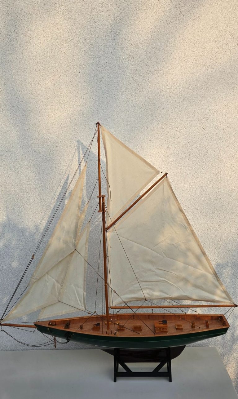 Modell eines Segelboots mit weißen Segeln und Holzdetails auf schwarzem Standfuß.