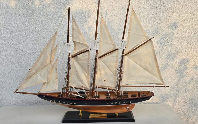 Modell eines Segelboots mit weißen Segeln und Holzdetails auf schwarzem Standfuß.
