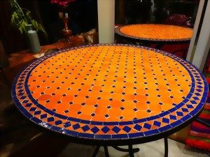 Runder Tisch mit orangefarbener Mosaikoberfläche und blauen Akzenten.