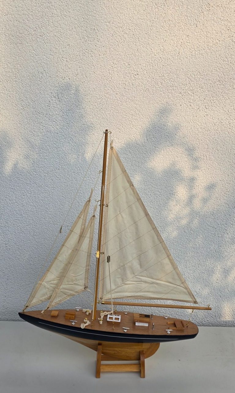 Modell eines Segelboots mit weißen Segeln und Holzdetails auf schwarzem Standfuß.