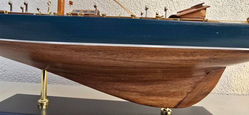 Modell eines Schiffs mit einem blauen Rumpf und einer hölzernen Unterseite.