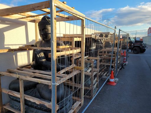 Lagerung von Buddha-Statuen in Holzkisten, umgeben von Bauzäunen und Baumaschinen.
