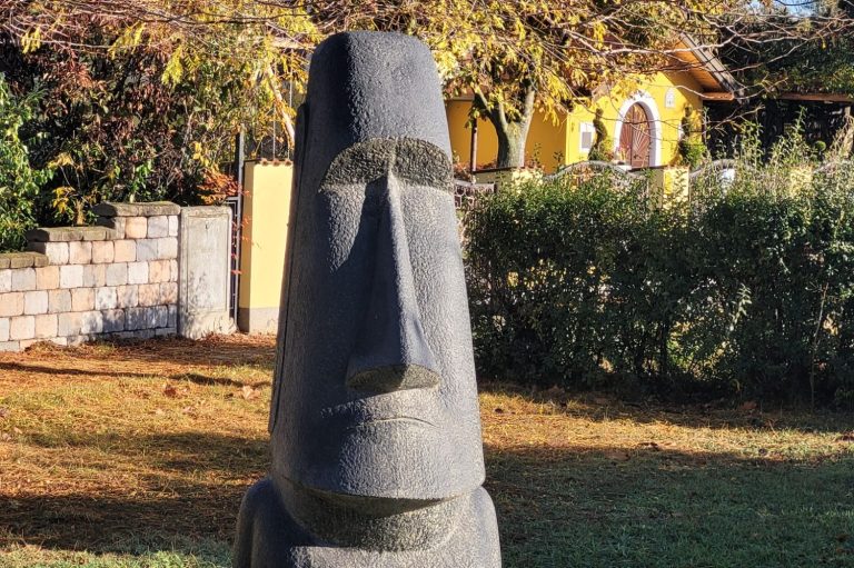Moai-Statue mit markanten Gesichtszügen vor einer bunten Hauskulisse.