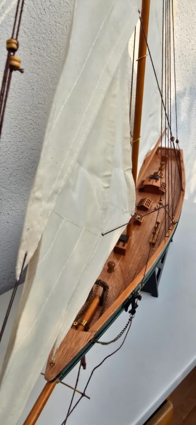 Ein Segelboot mit weißen Segeln und Holzteilen, schräg von der Seite aufgenommen.
