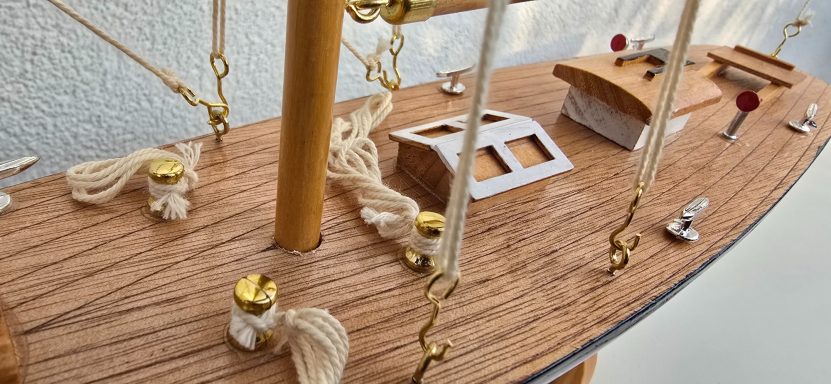 Modell eines Schiffs mit Holzdecks, Segeln und Detailteilen in Gold und Weiß.