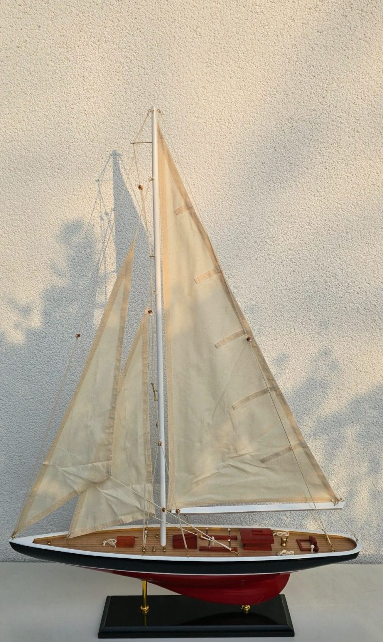 Modell eines Segelboots mit weißen Segeln und Holzdetails auf schwarzem Standfuß.