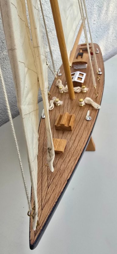Detailreiche Miniatursegelyacht mit Holzdeck und weißen Segeln.