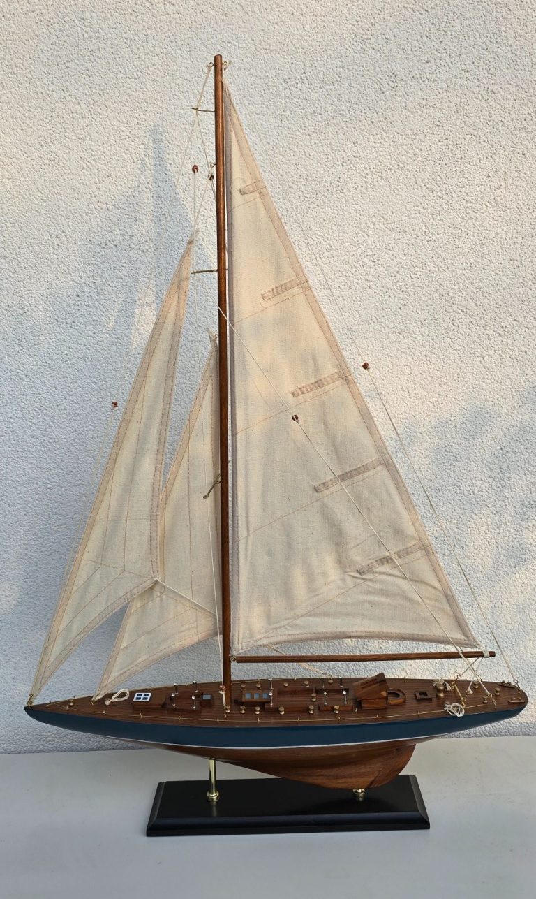 Modell eines Segelboots mit weißen Segeln und Holzdetails auf schwarzem Standfuß.