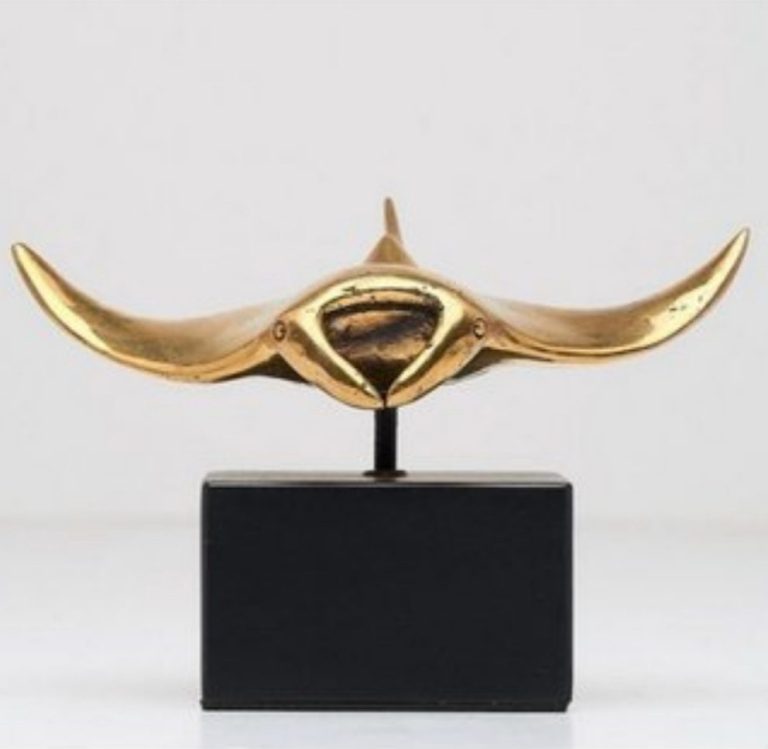 Goldene Skulptur mit geschwungener Form auf schwarzem Sockel.