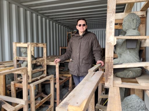 Person steht in einem Container umgeben von Holzregalen mit Skulpturen.