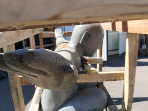 Skulptur eines humanoiden Körpers mit ausgestreckten Armen, auf einer Holzstruktur.