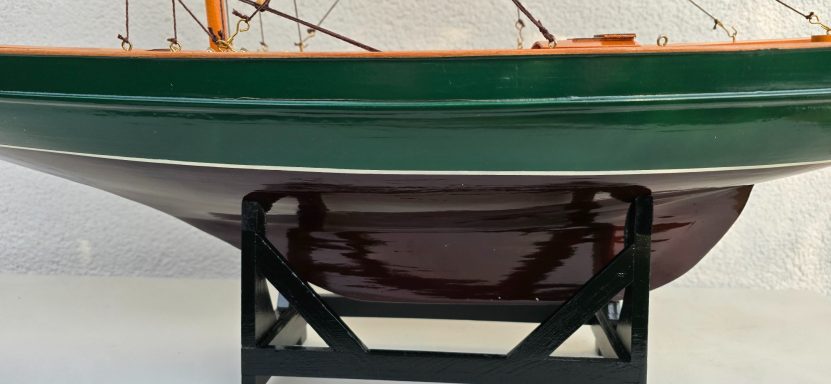 Modell eines Schiffes in Grün und Rot auf einem Ständer, seitliche Ansicht.