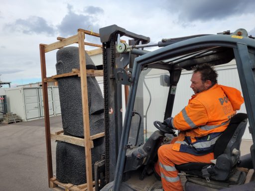 Ein Mann in orangefarbener Arbeitskleidung fährt einen Gabelstapler mit einer Last.