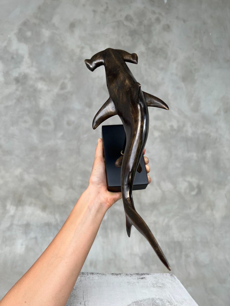 Bronzefigur eines Haifischs auf schwarzem Sockel.