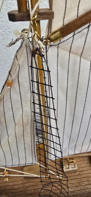 Seilnetz an einem Schiffsmast mit Holzdetails und gestreiftem Segel.