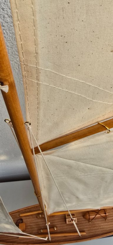 Detailansicht eines Segelboots mit hölzernen Mast und weißen Segeln.