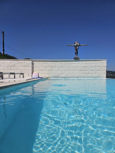 Ein Pool mit klarem Wasser und einer Statue im Hintergrund vor blauem Himmel.