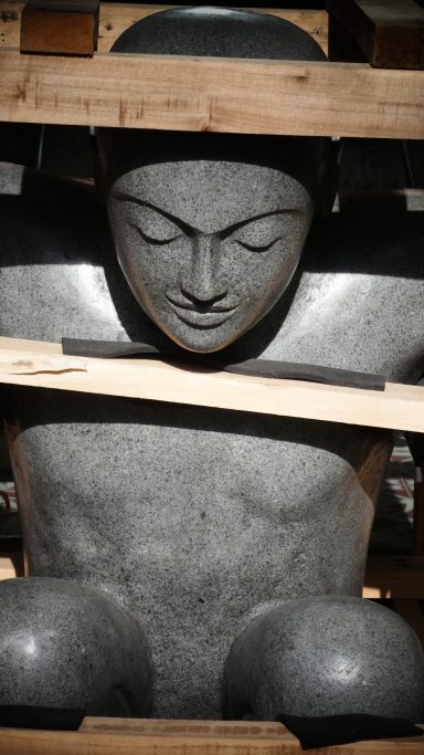 Skulptur eines sitzenden menschlichen Körpers, teilweise von Holzlatten umgeben.