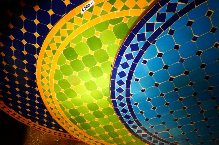 Bunte, geometrische Muster in Blau, Grün und Gelb auf runden Tischflächen.