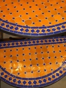 Detailreiche, orange und blaue Mosaik-Fliesen auf zwei runden Tischplatten.