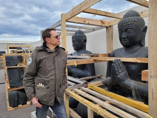 Mann steht neben Lagerstatue eines Buddha, umgeben von Holzgestellen.