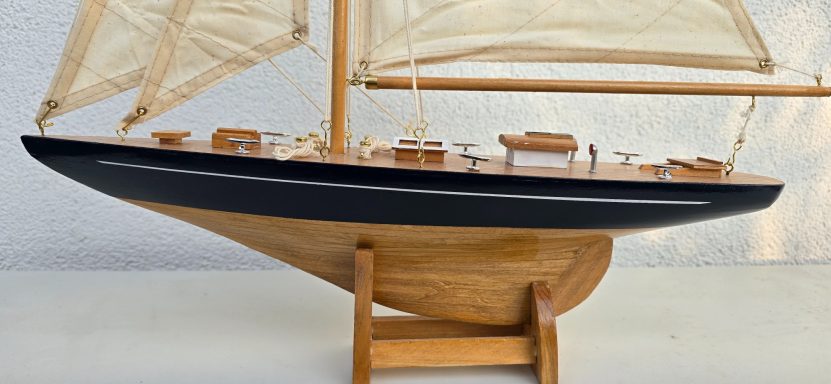 Modell eines Segelbootes mit Holzdeck und weißen Segeln, auf einem Holzgestell.
